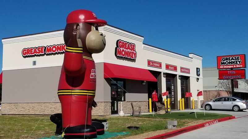 A large inflatable monkey mascot stands in front of a Grease Monkey auto center.