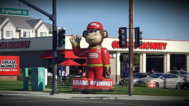 A giant inflatable monkey mascot stands in front of a new Grease Monkey auto service center.
