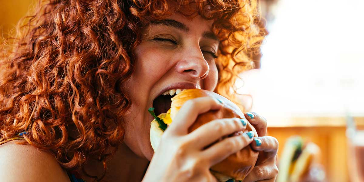 A red-haired girl is eating a cheeseburger.