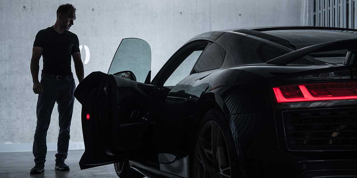 In a garage, man stands near a sports car that has the driver's side door open.